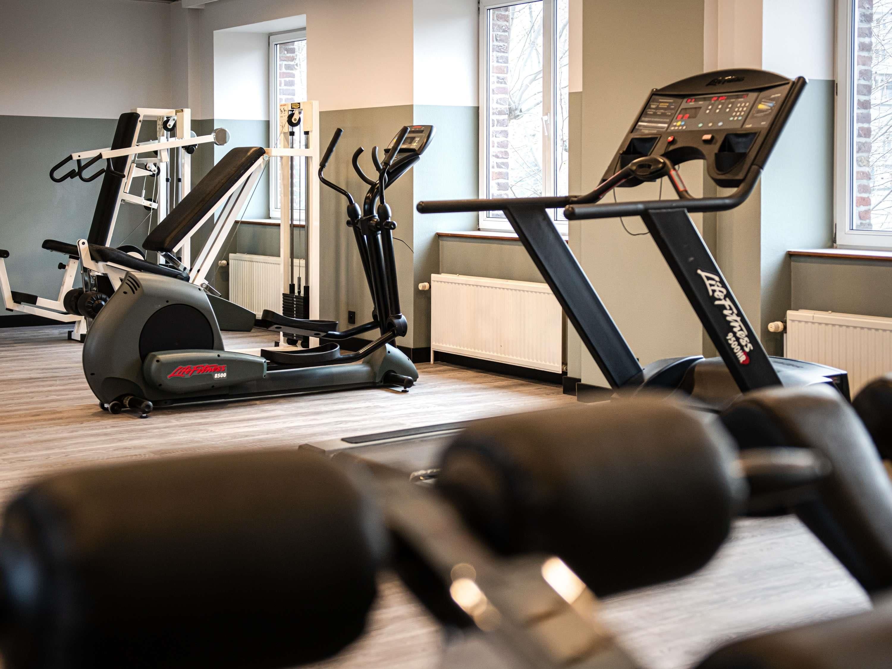 A gym with cardio machines, dumbbells, and a window with a view.