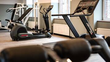 A gym with cardio machines, dumbbells, and a window with a view.
