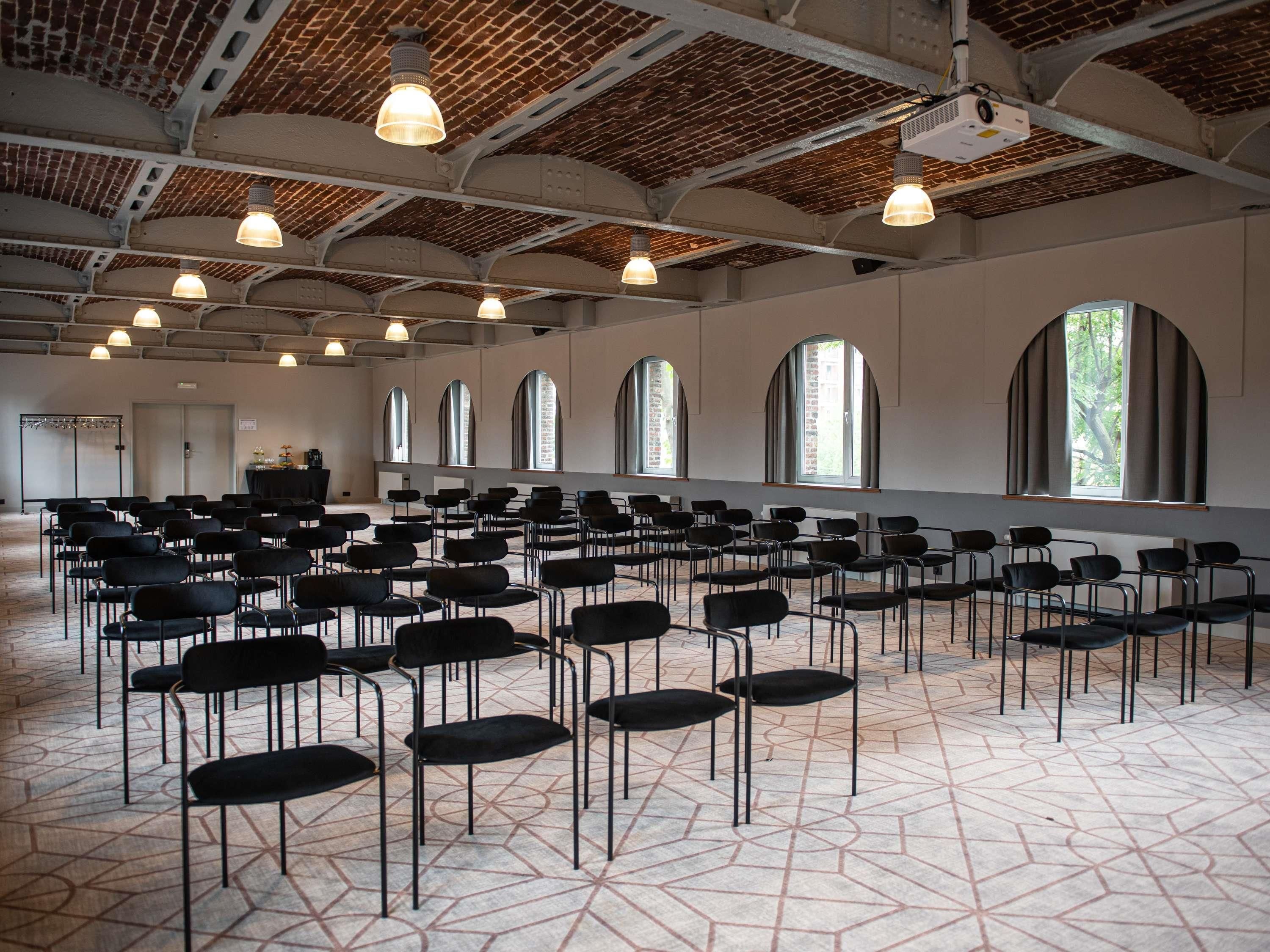 Een vergaderzaal met rijen stoelen, gebogen ramen en een projector aan het plafond.