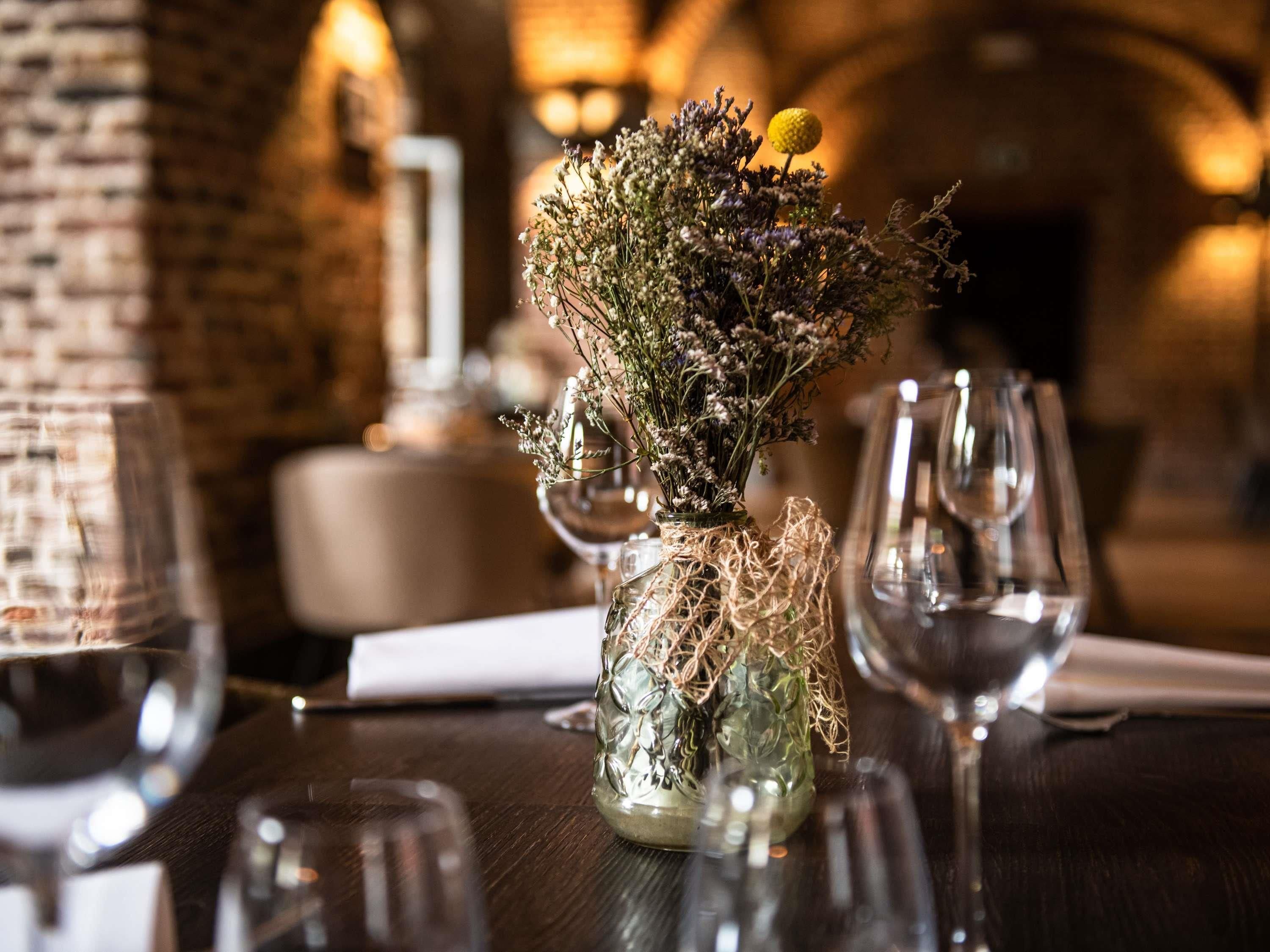 Een tafel met een glazen vaas met gedroogde bloemen en een klein, geel voorwerp, omringd door wijnglazen.