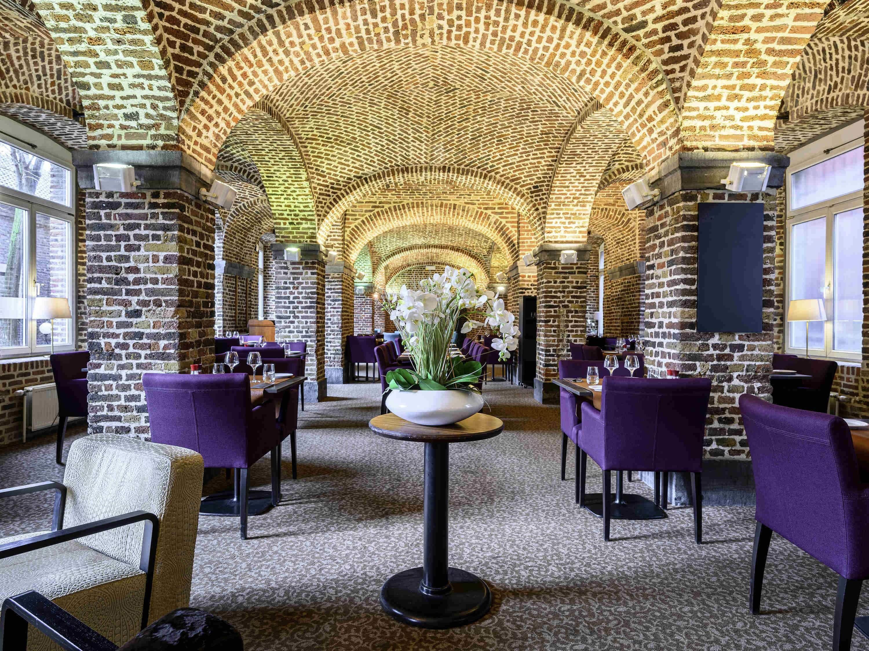 A restaurant with brick arches, purple chairs, and a central table with flowers.