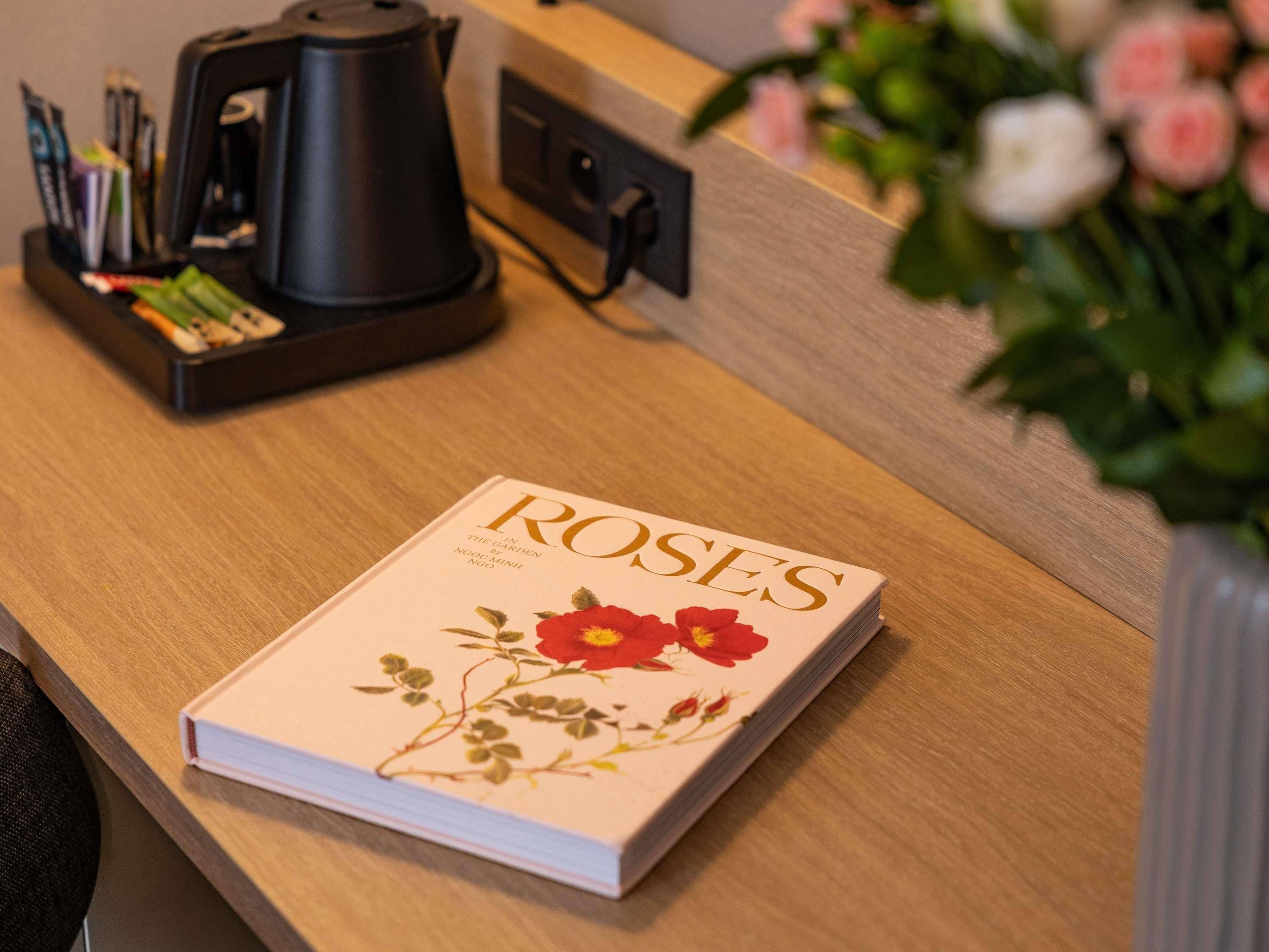 A book titled 'ROSES' on a wooden desk with a coffee maker and pens in a holder.