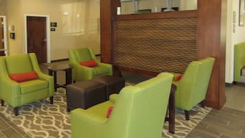 A lobby with green armchairs, a coffee table, and a patterned rug.