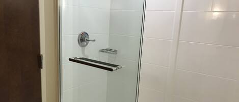 A glass-enclosed shower stall with a chrome faucet and a glass shelf.