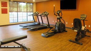 Un gimnasio con cintas de correr, elíptica y un banco.