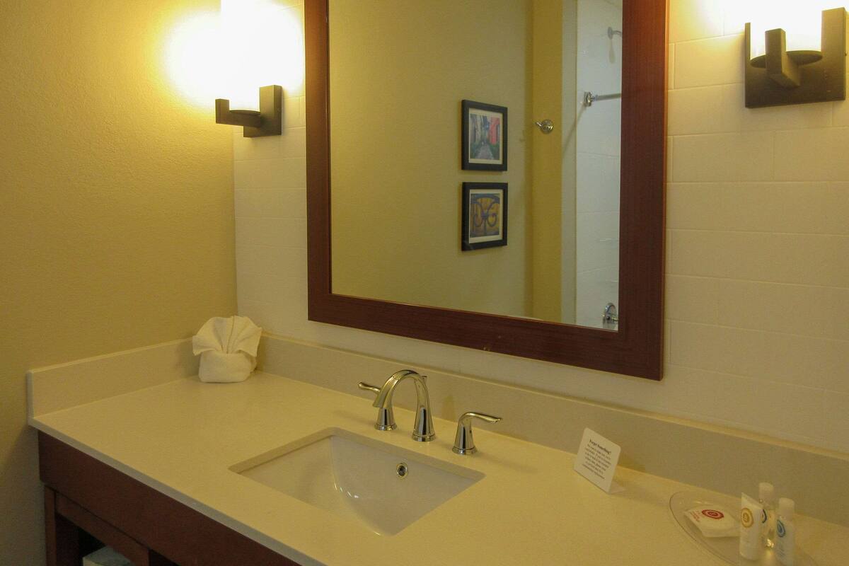 A hotel bathroom with a double sink, a large mirror, and a towel dispenser.