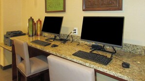 Un escritorio con dos monitores, un teclado y un ratón. Hay dos sillas, una impresora y dos botellas de agua sobre el escritorio.