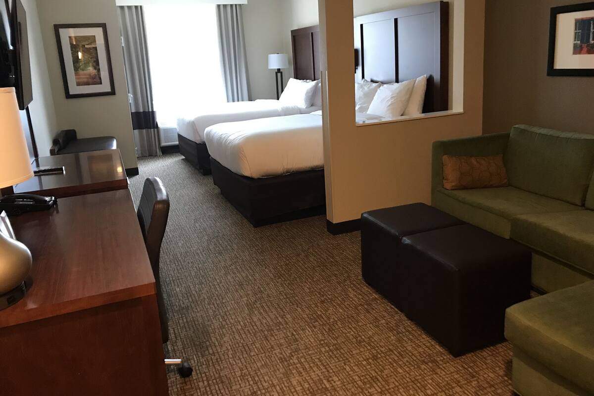 A hotel room with two beds, a desk, a couch, and a mirror.