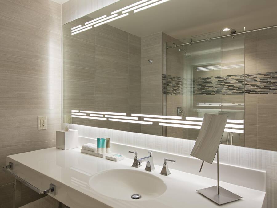 Une salle de bain moderne avec un grand miroir, un lavabo blanc et une cabine de douche en verre.