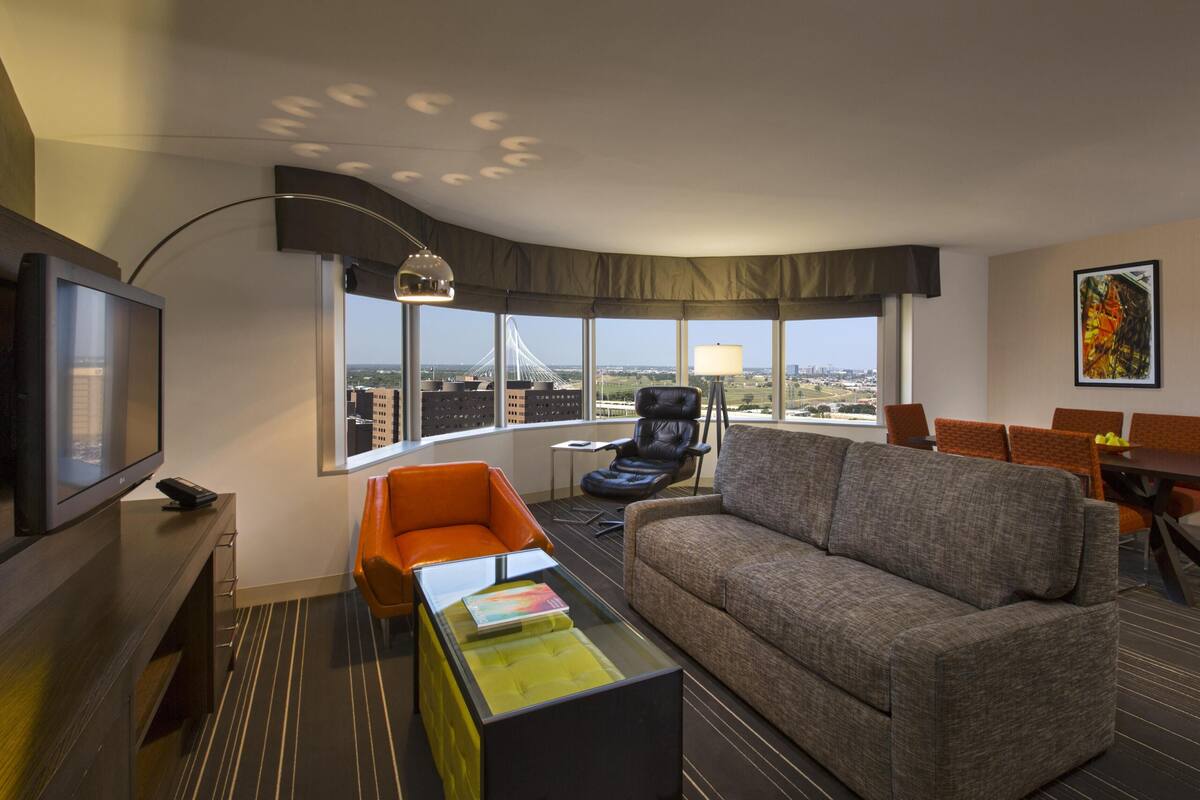 Une chambre d’hôtel dotée d’une grande fenêtre, d’une télévision, d’un canapé, d’une table basse et d’un coin repas.