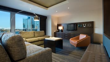 A modern hotel room with a sofa, armchair, and a flat-screen TV mounted on the wall.