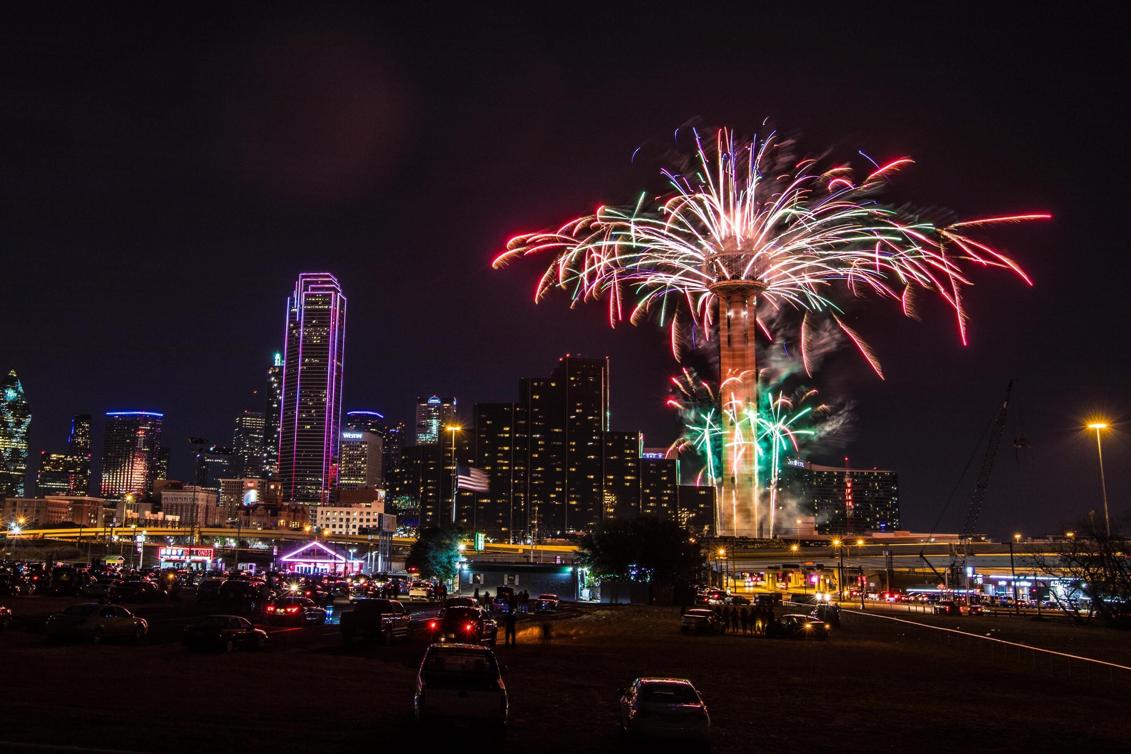 A city skyline with illuminated buildings and a large fireworks display.
