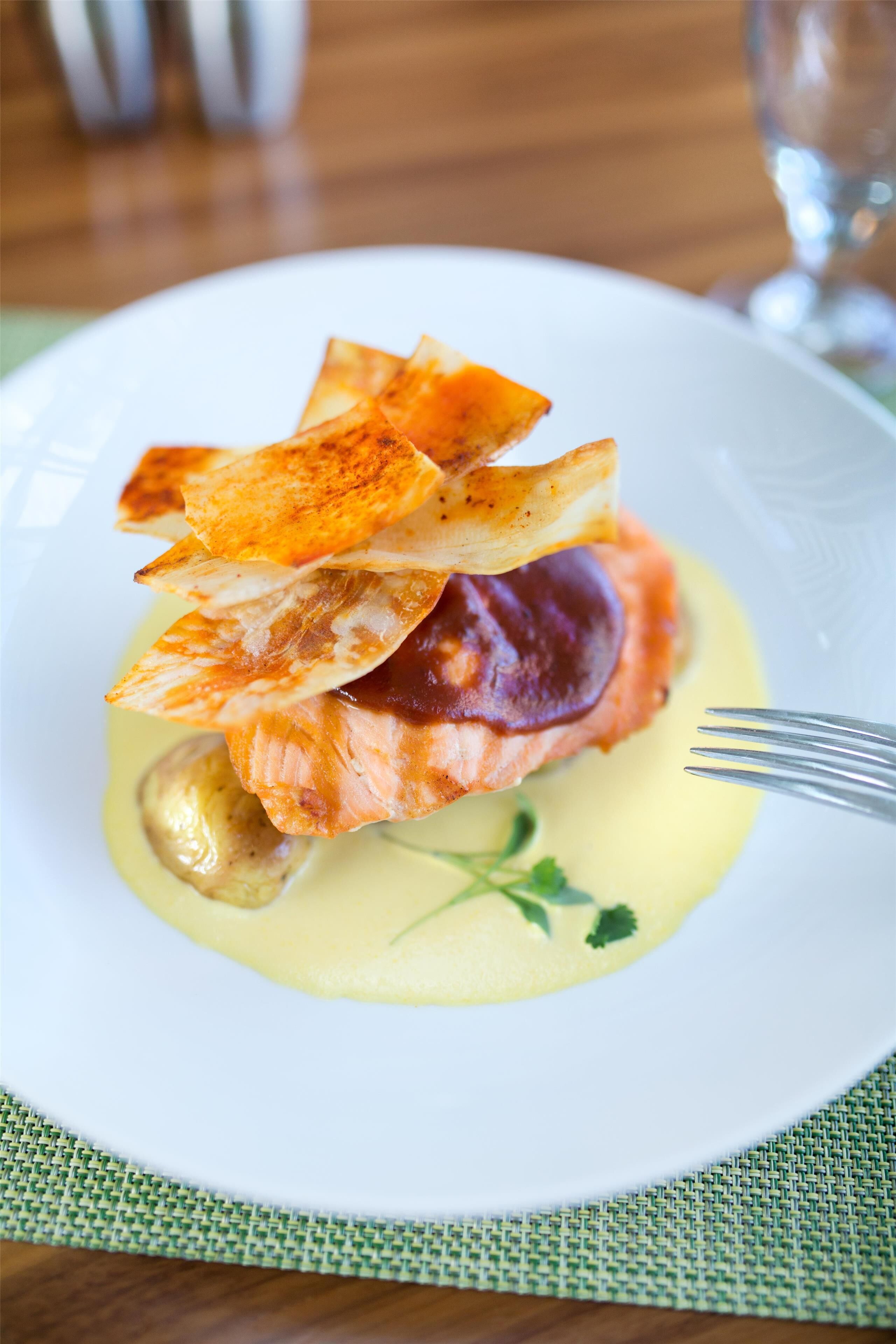 A plate with a piece of salmon, a slice of lemon, and a fork on a table.