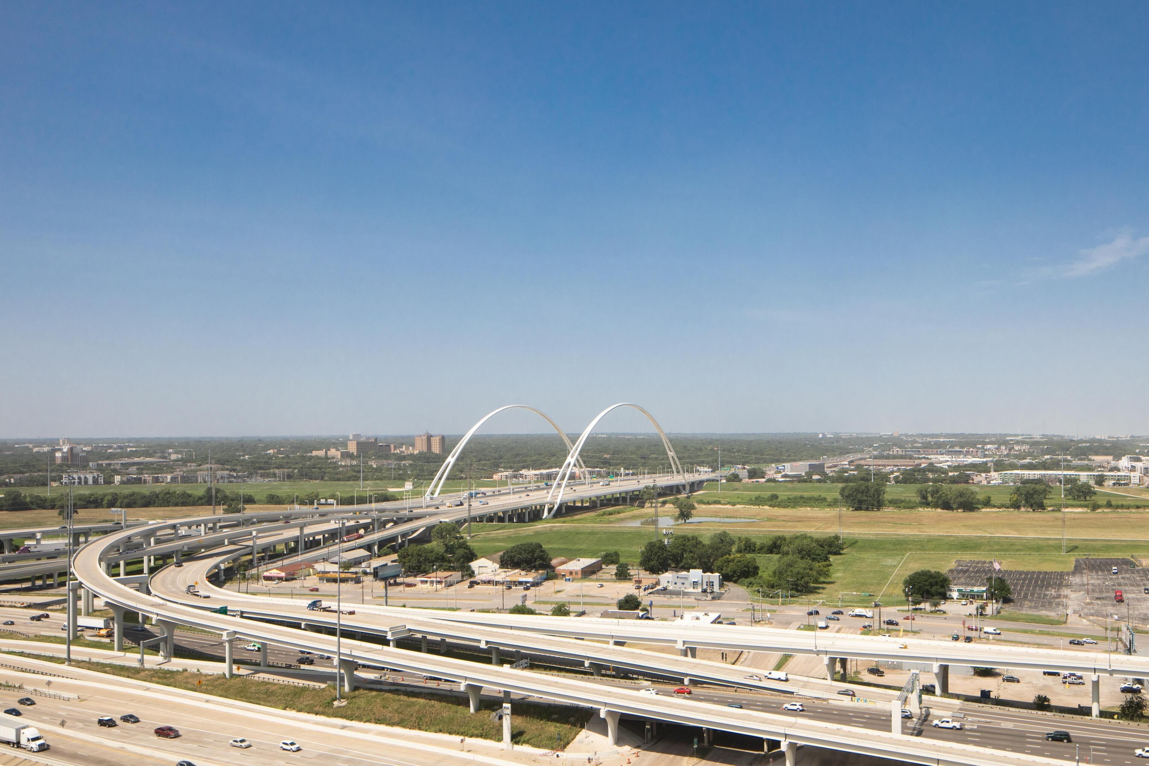 Un intercambio de autopistas de varios niveles con pasos elevados y un gran puente blanco al fondo.