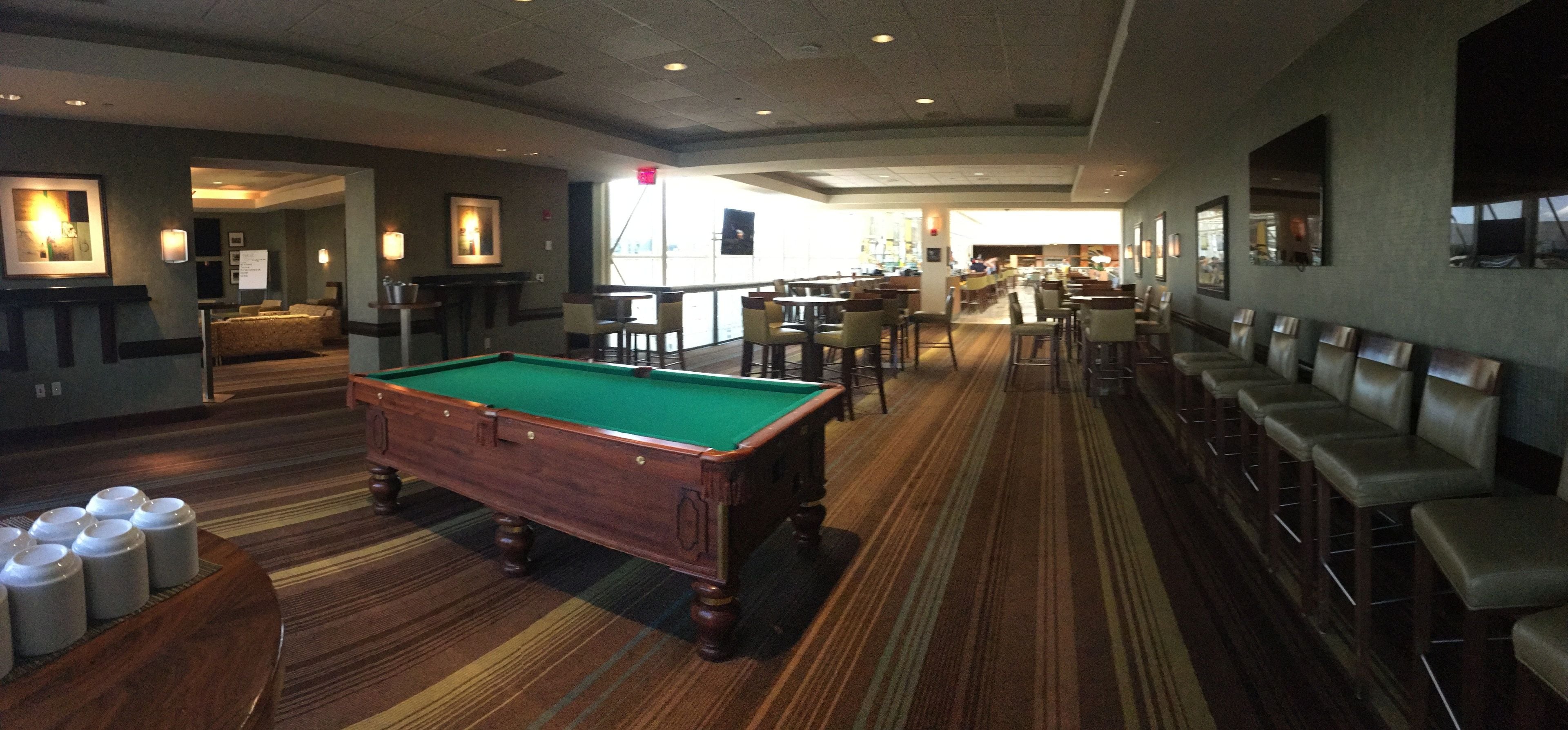 Een pooltafel in een hotel lobby, met een bar en zitplaatsen.