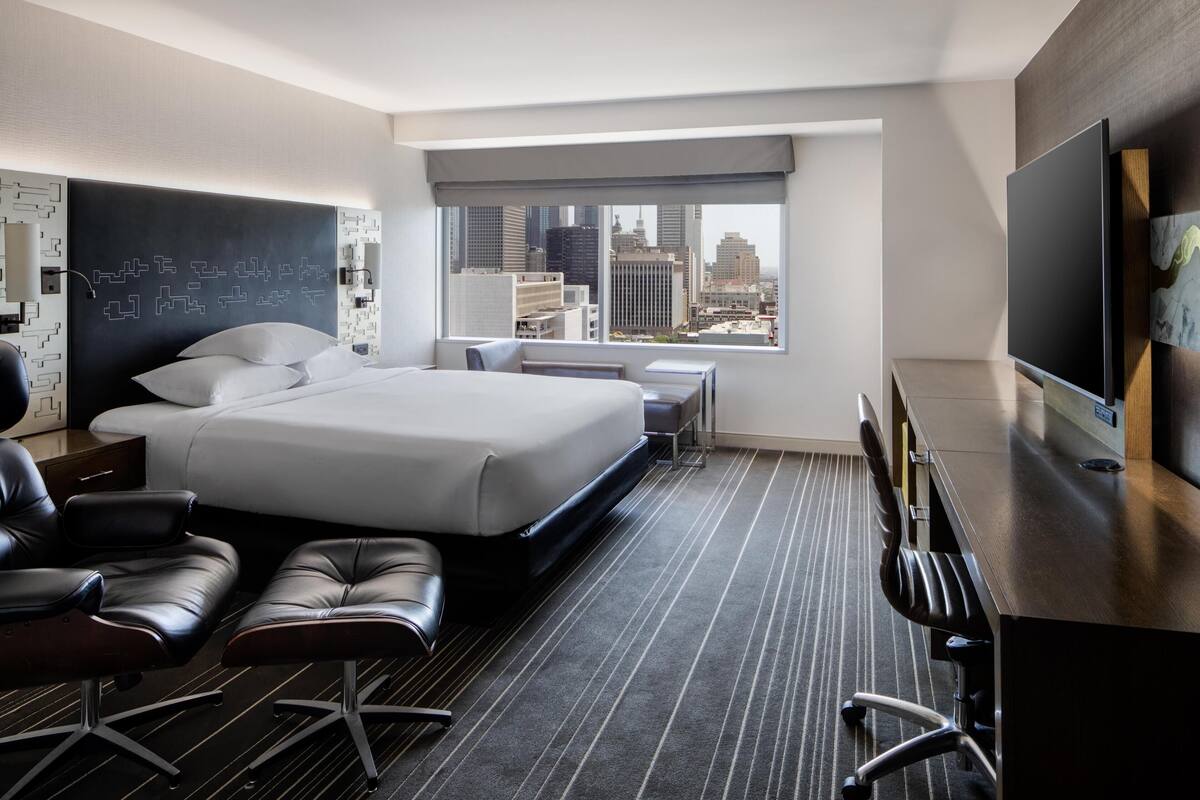 Une chambre d’hôtel avec un grand lit, un bureau, une chaise, une télévision et une vue sur la ville.