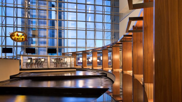 A modern hotel lobby with a central water feature, large glass windows, and wooden paneling.