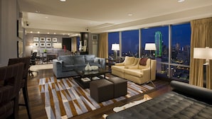A modern hotel room with a city view, a sofa, a coffee table, and a dining area.