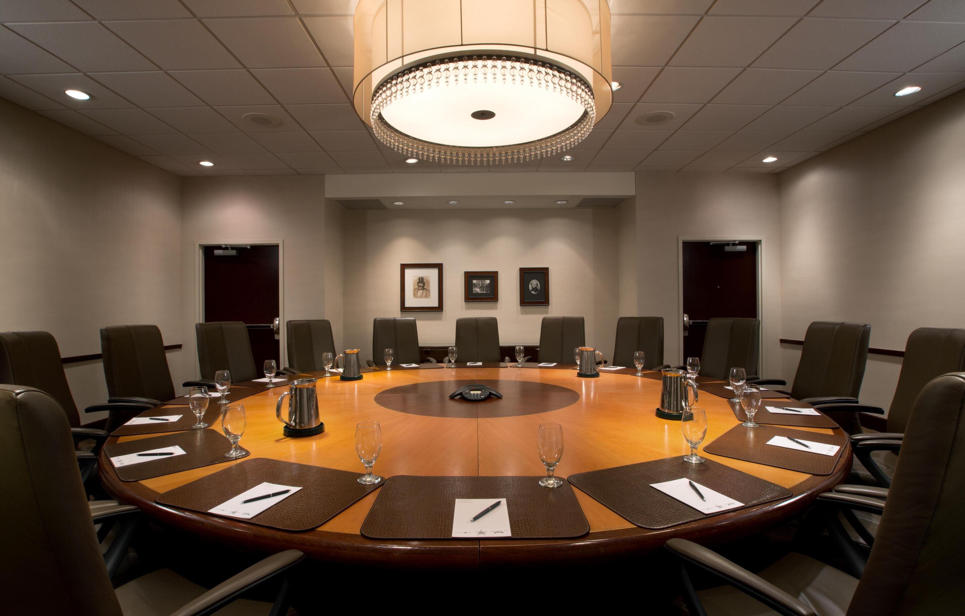Un salón de conferencias con una mesa redonda, sillas, una lámpara de araña y cuadros en la pared.