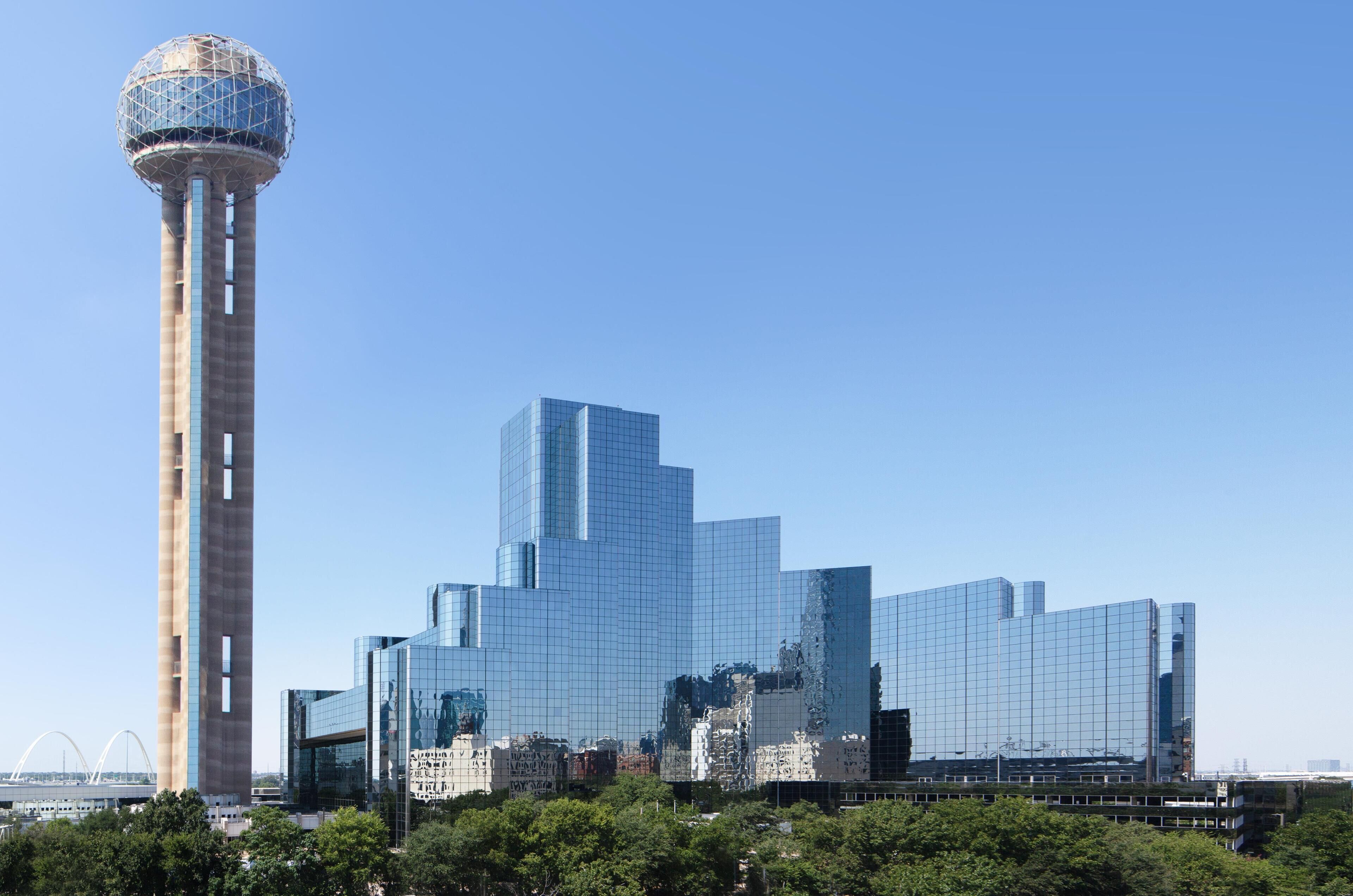 Un rascacielos moderno con fachada de vidrio y una torre cilíndrica con cúpula esférica.