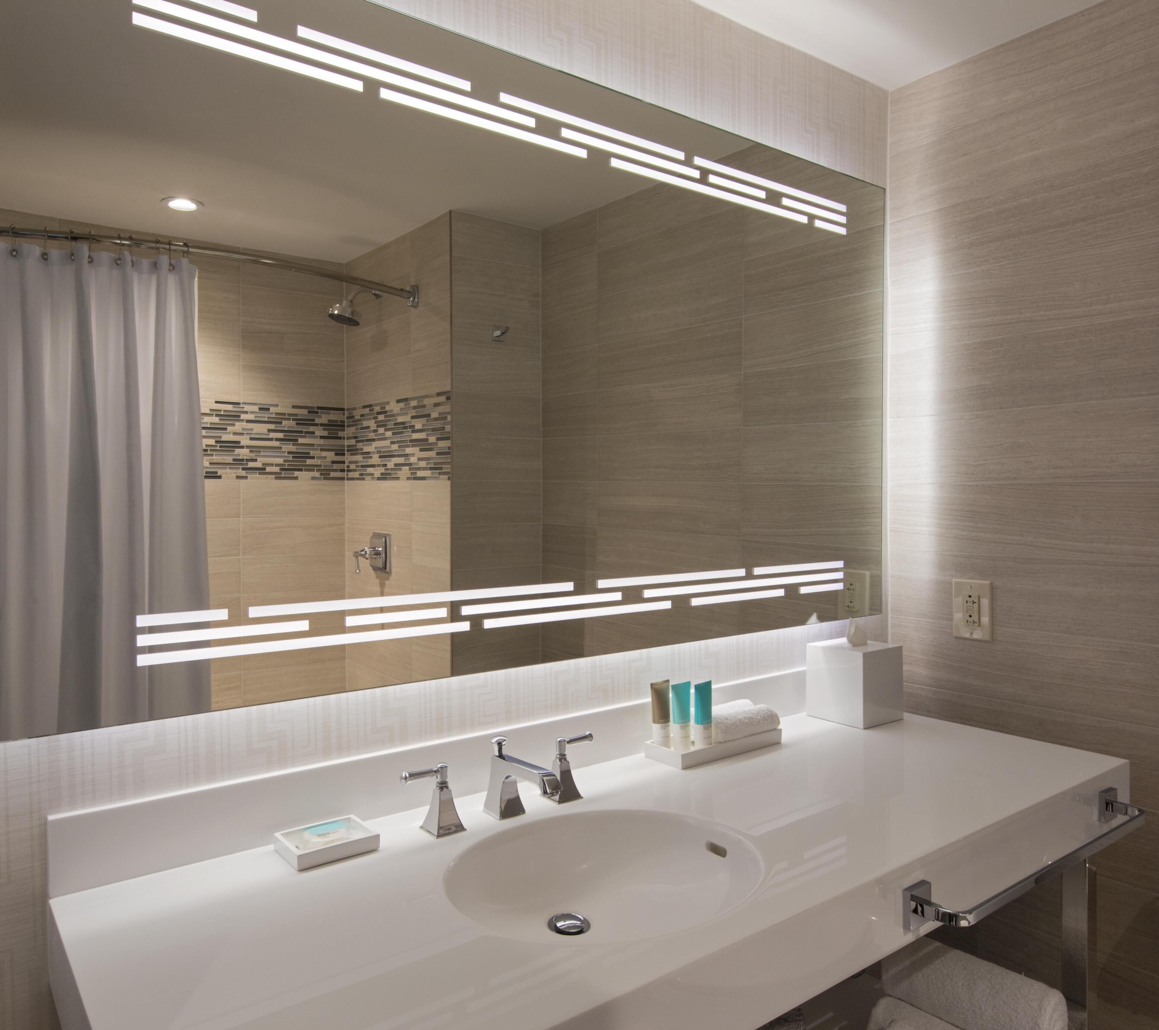 A modern bathroom with a large mirror, a white sink, and a shower area.