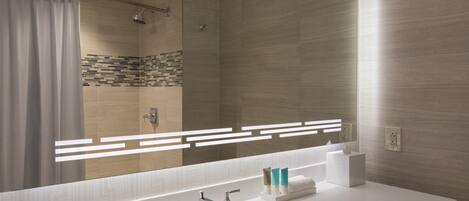 A modern bathroom with a large mirror, a white sink, and a shower area.