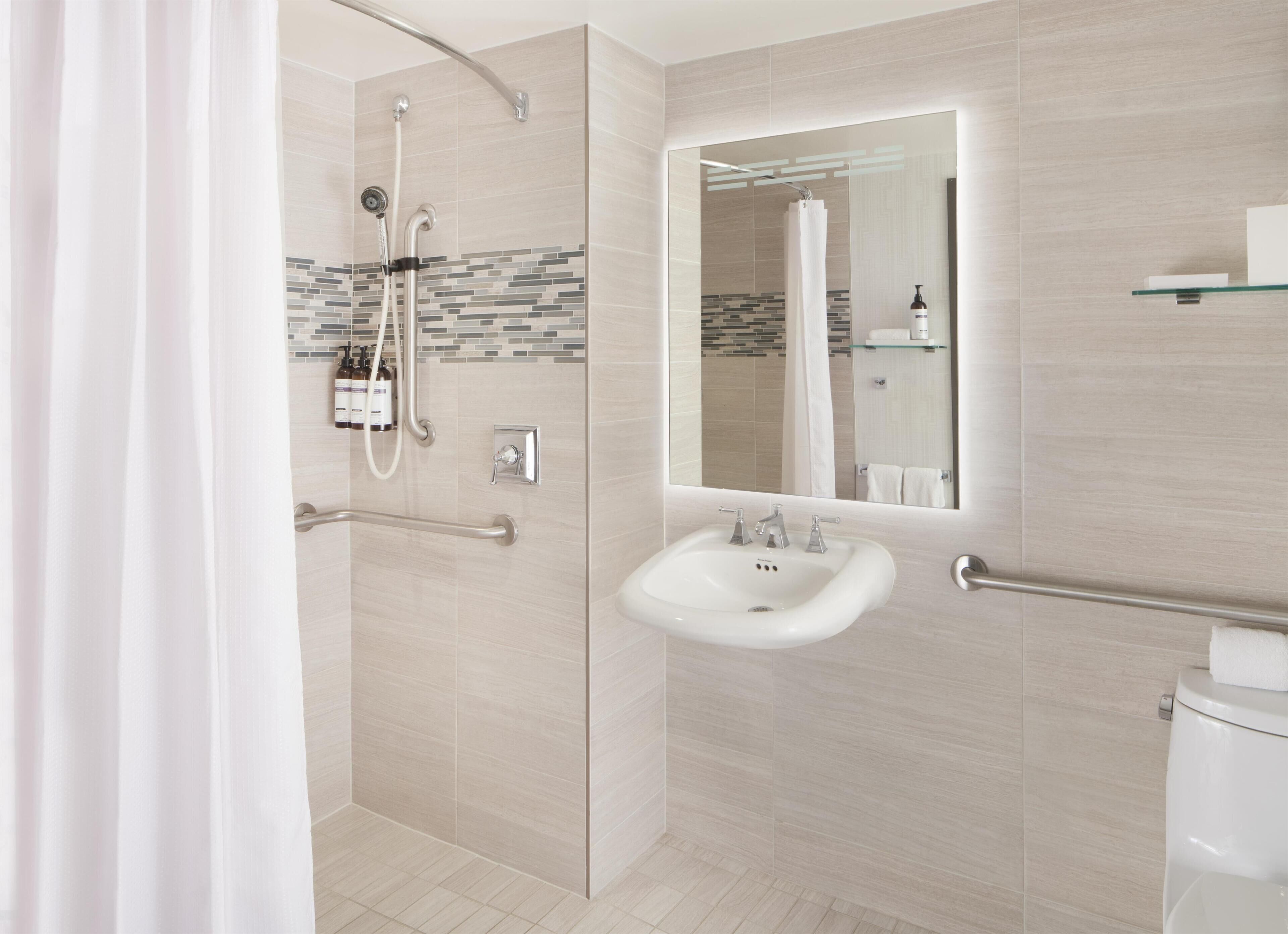 Une salle de bain moderne dotée d’une douche à l’italienne, de toilettes séparées par une paroi en verre et d’un meuble-lavabo avec un miroir.