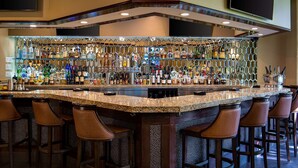 Zona de bar con encimera de granito, varias botellas de licor y taburetes.