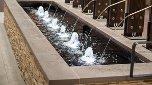 Una fuente de agua interior moderna con múltiples chorros, rodeada de paneles de madera y zonas de estar.