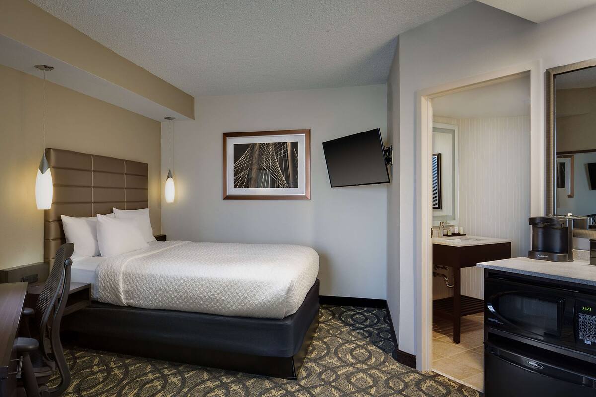 Habitación de hotel con cama, escritorio, silla, televisión de pantalla plana y kitchenette.