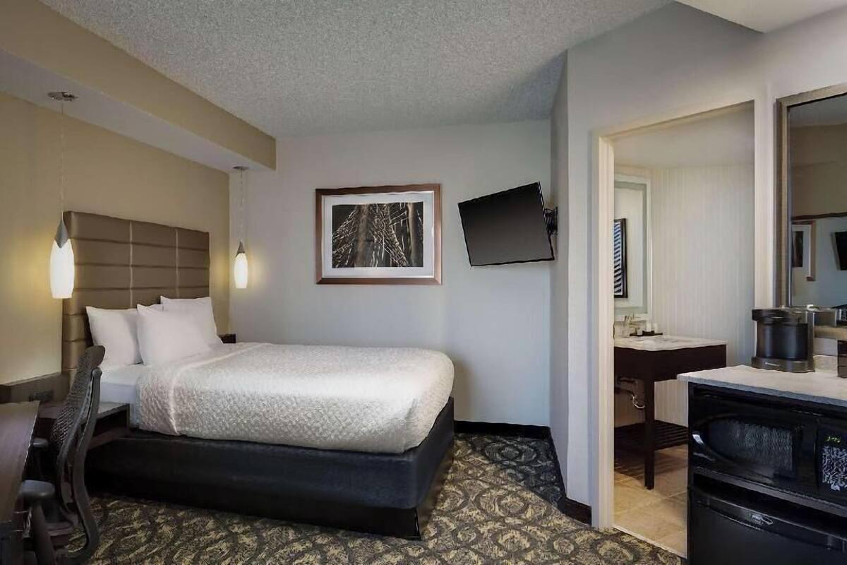 Habitación de hotel con cama, escritorio, silla, televisor de pantalla plana y cafetera.