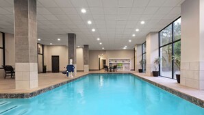 Una piscina interior con paredes y techo azulejados, un área de recepción con sillas y mostrador, y ventanas amplias a un lado.