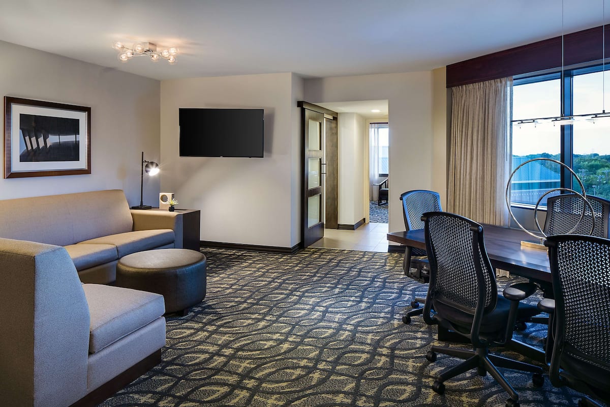 Habitación de hotel con sofá, televisión de pantalla plana, escritorio y sillas, y alfombra estampada.