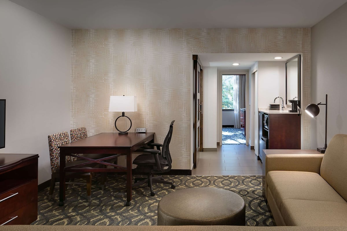 Habitación de hotel con televisión, escritorio con lámpara, sofá y área de cocina con fregadero y microondas.