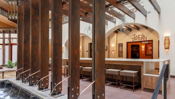 Un interior moderno con una zona de bar, vigas de madera y una fuente de agua.
