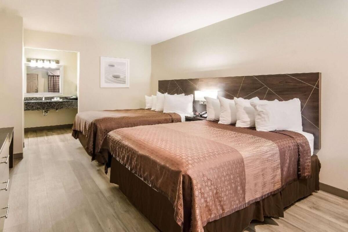 A hotel room with two beds, a bathroom with a mirror, and a small desk.