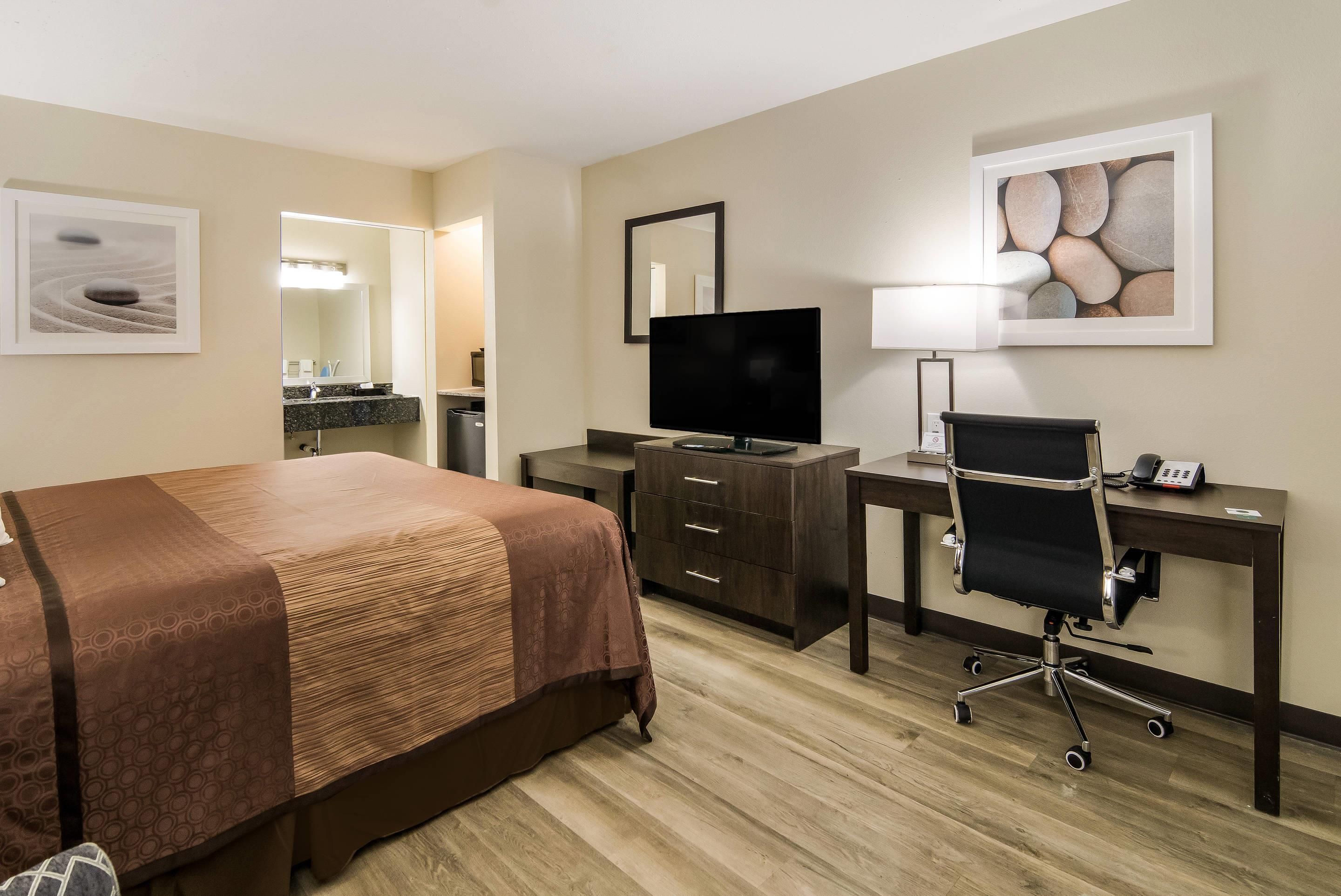 A hotel room with a bed, desk, chair, television, and artwork on the walls.