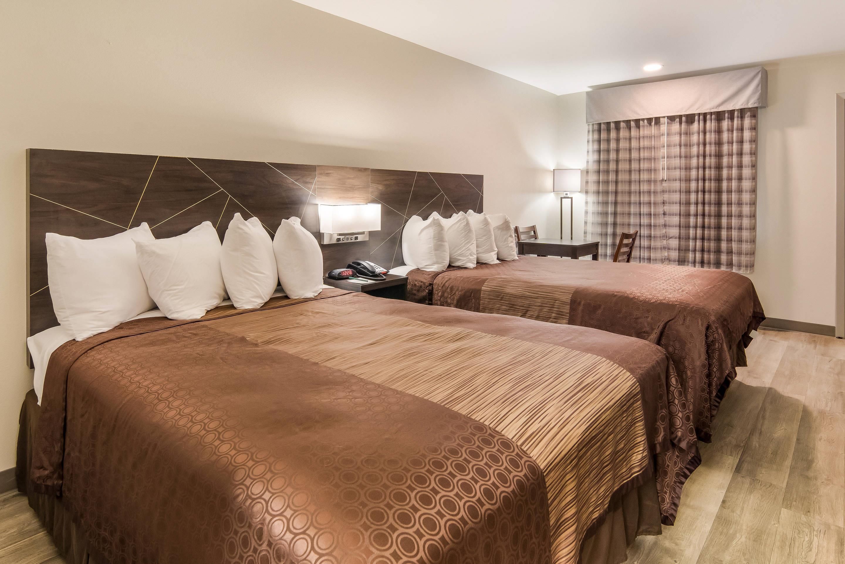 Une chambre d’hôtel avec deux lits, une table de chevet avec un téléphone, une lampe et une fenêtre avec des rideaux.