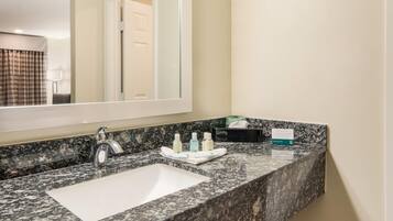 Un baño con lavabo de mármol, un espejo y artículos de aseo en la encimera.