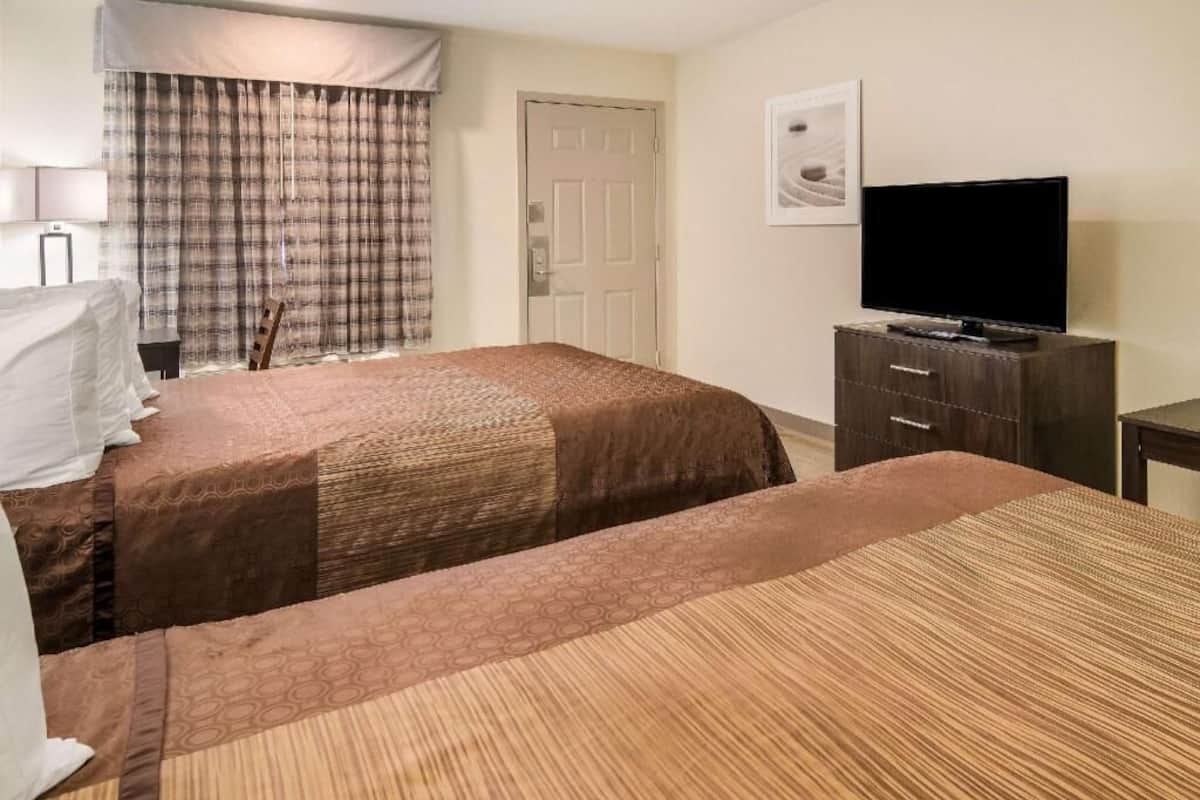 A hotel room with two beds, a television, a dresser, and a door.