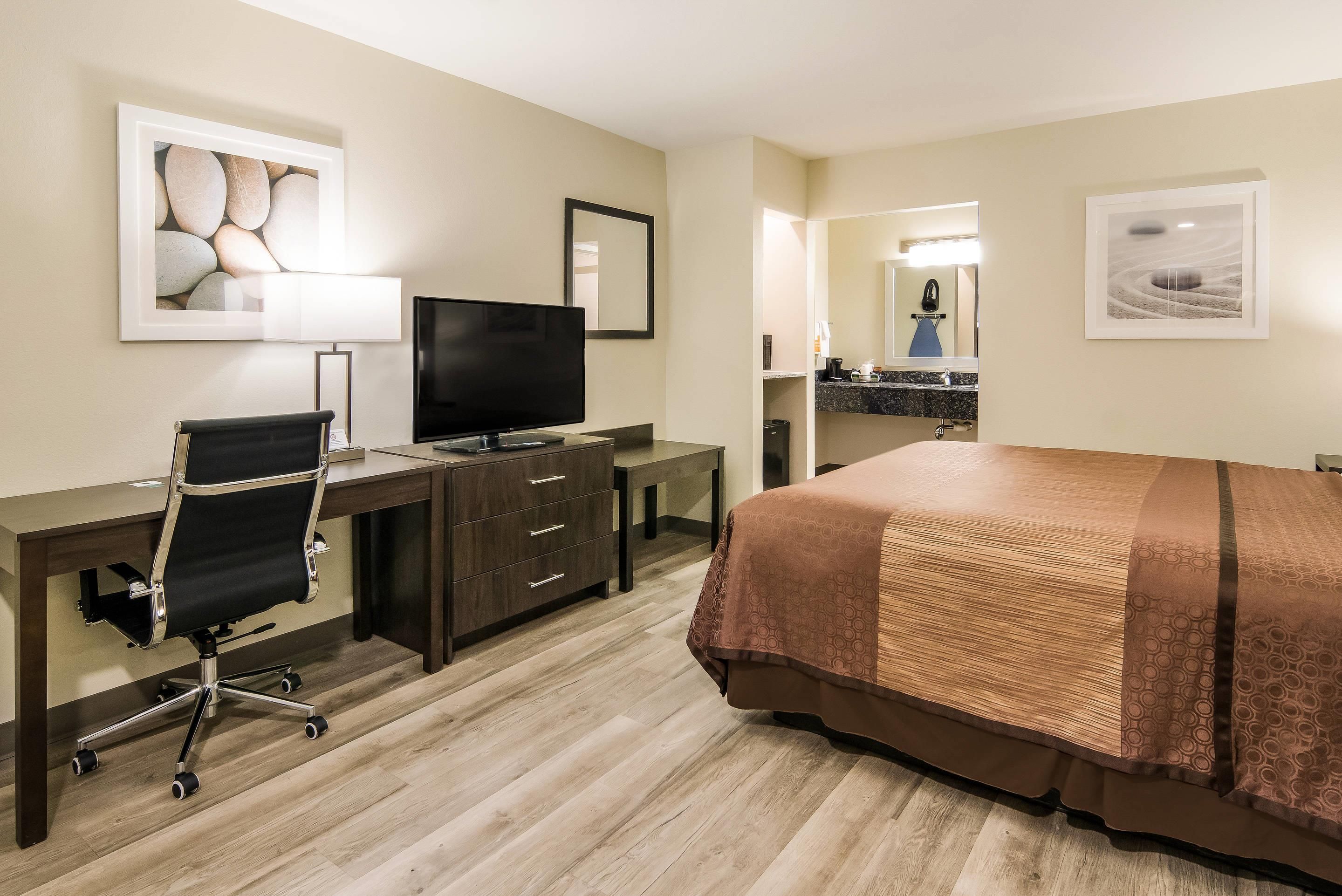 A hotel room with a bed, desk, chair, television, and artwork on the walls.