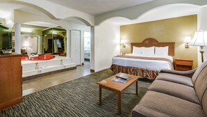 A hotel room with a bed, a sofa, a small table, a mirror, a dresser, and a bathroom visible through an archway. - Quality Inn & Suites Dallas - Cityplace (Dallas)