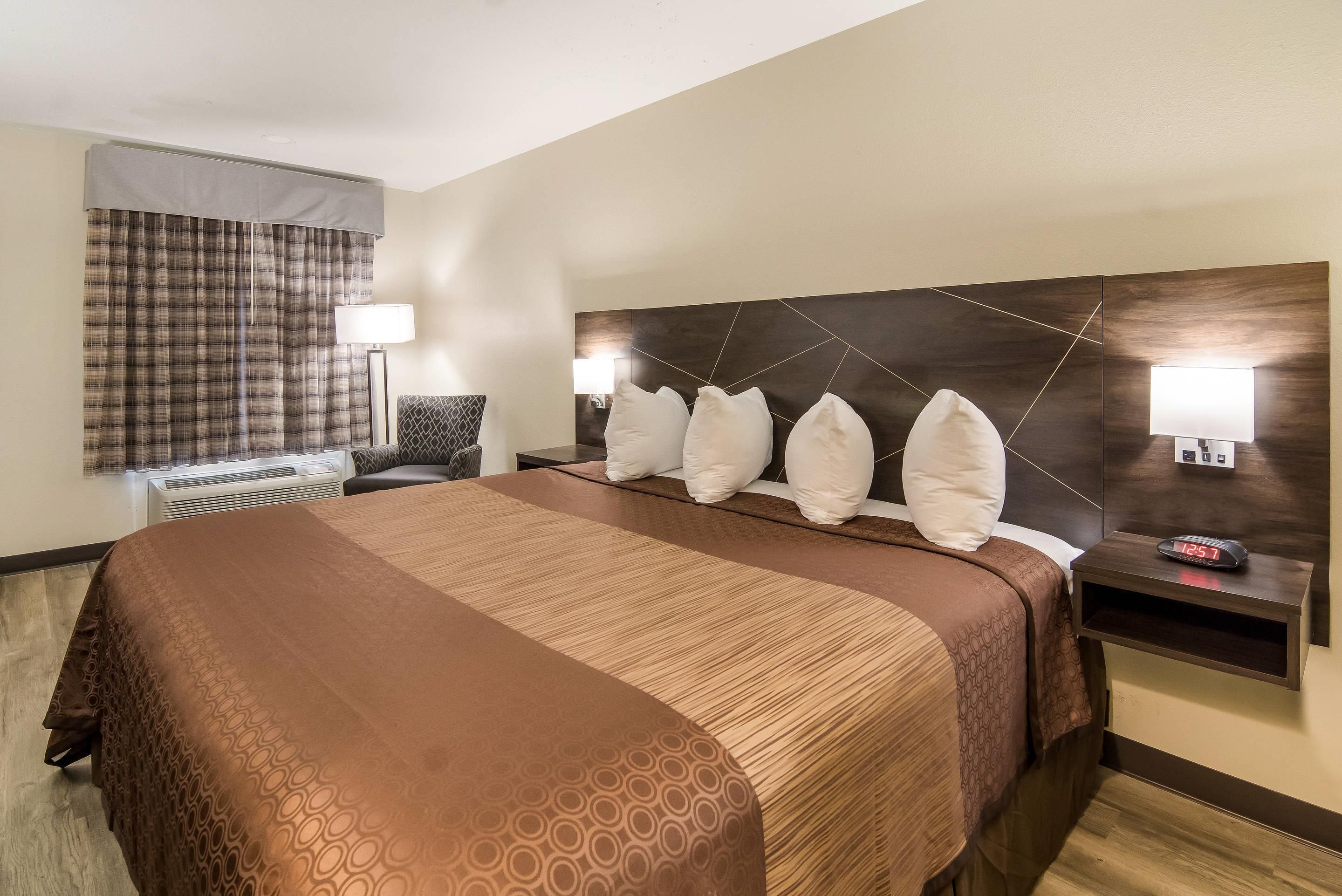 Ein Hotelzimmer mit einem großen Bett, zwei Nachttischen mit Lampen, einem Kopfteil mit geometrischen Mustern und einem Fenster mit Vorhängen.
