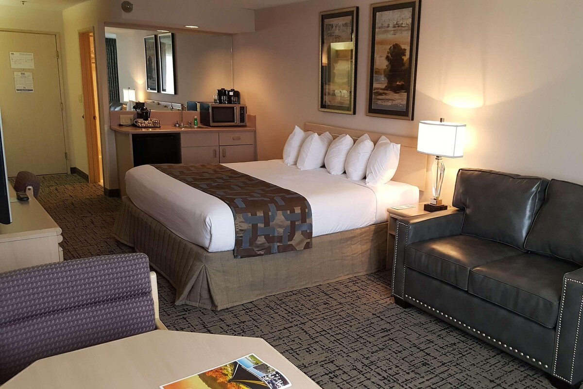 A hotel room with a bed, a black leather sofa, a desk with a lamp, a microwave, and a small cabinet.