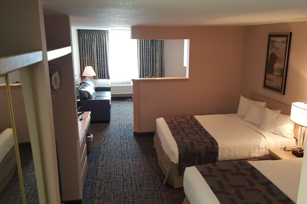 A hotel room with a bed, a desk, a chair, a window, and a painting on the wall.
