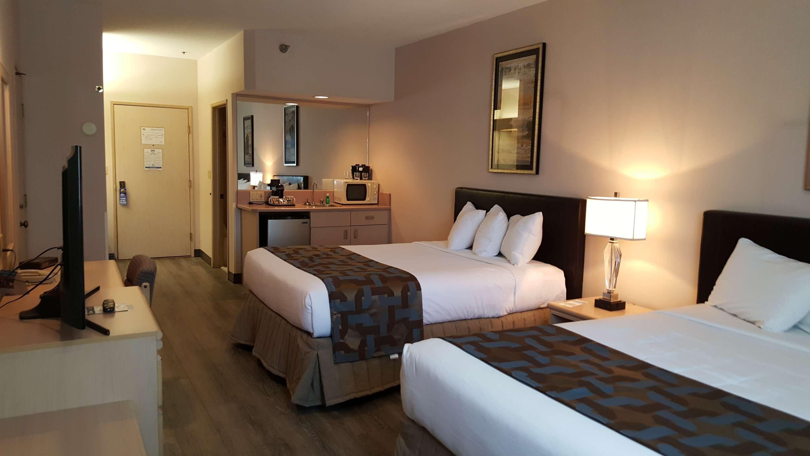 A hotel room with two beds, a desk with a computer, a microwave, and a small kitchenette.