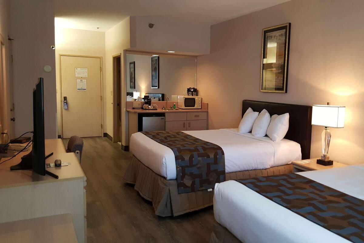 A hotel room with two beds, a desk with a computer, a microwave, and a small kitchenette.