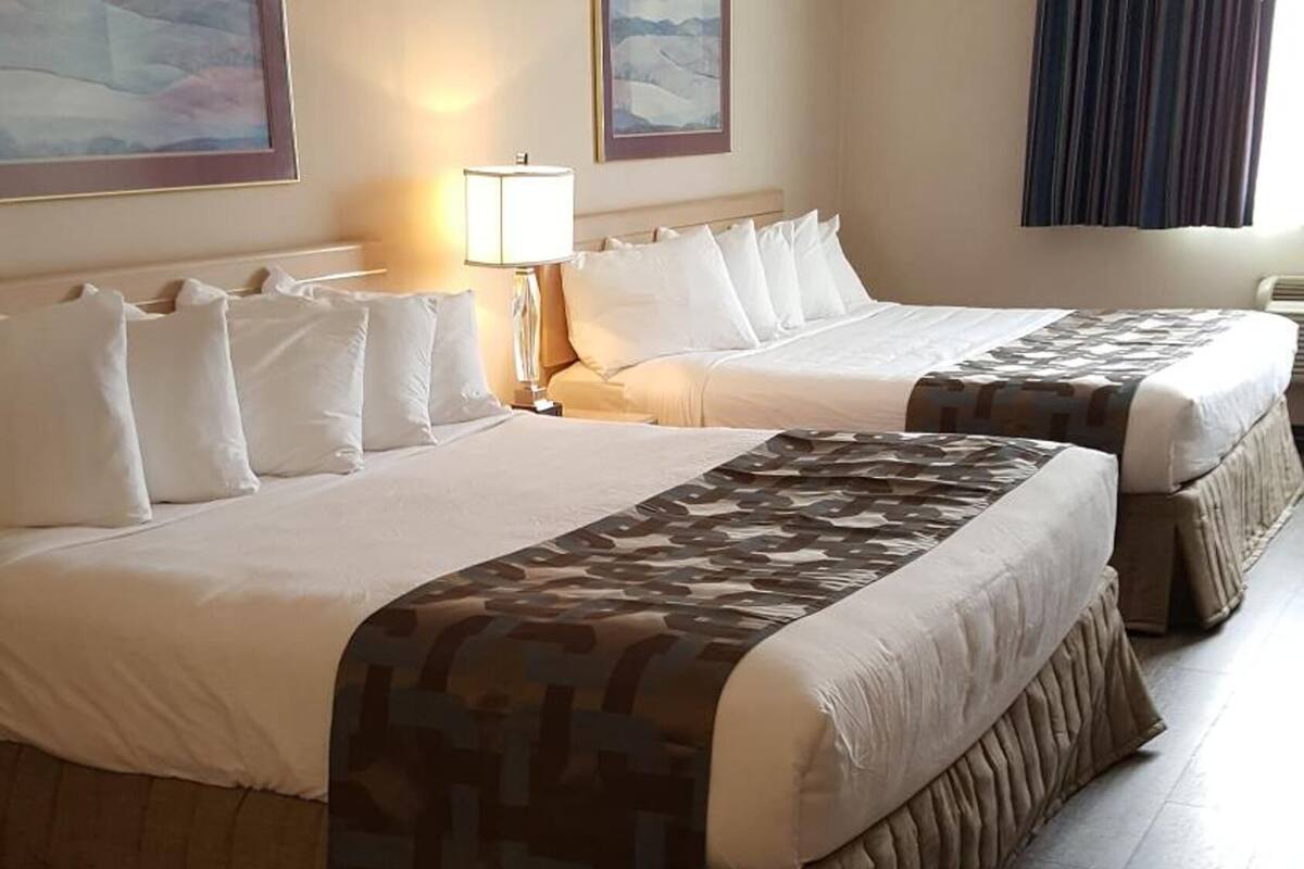 A hotel room with two beds, a large window with curtains, and a painting on the wall.