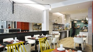A modern restaurant with white and yellow chairs, black tables, and a kitchen area in the background. - Hôtel Haussmann Saint Augustin (Paris)
