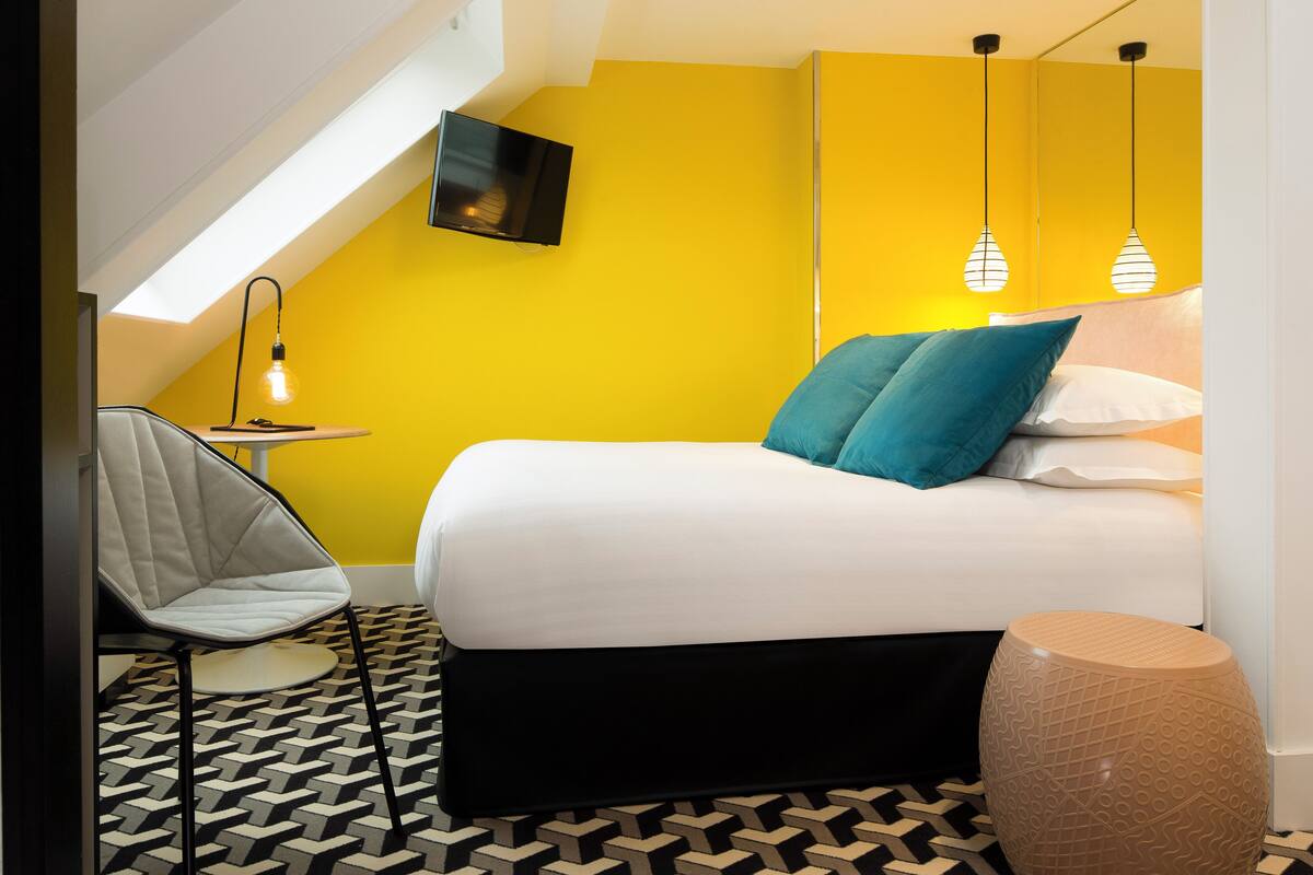 A modern bedroom with a bed, a chair, a TV, and pendant lights.